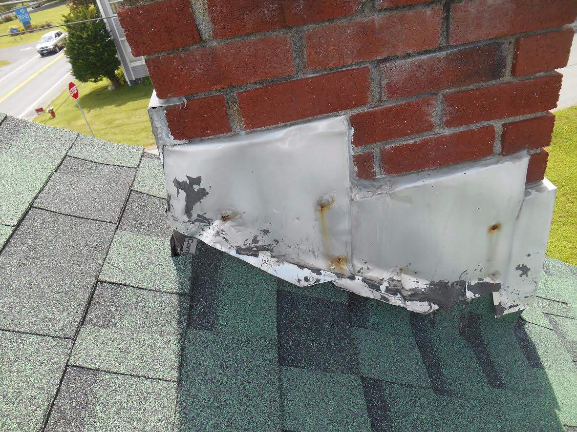Damaged metal flashing at a brick chimney where it meets asphalt shingles