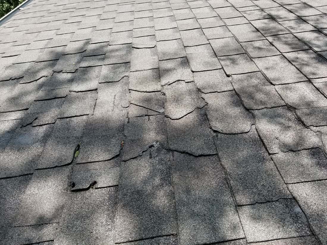 Broken and curling asphalt shingles with missing corners on a worn roof