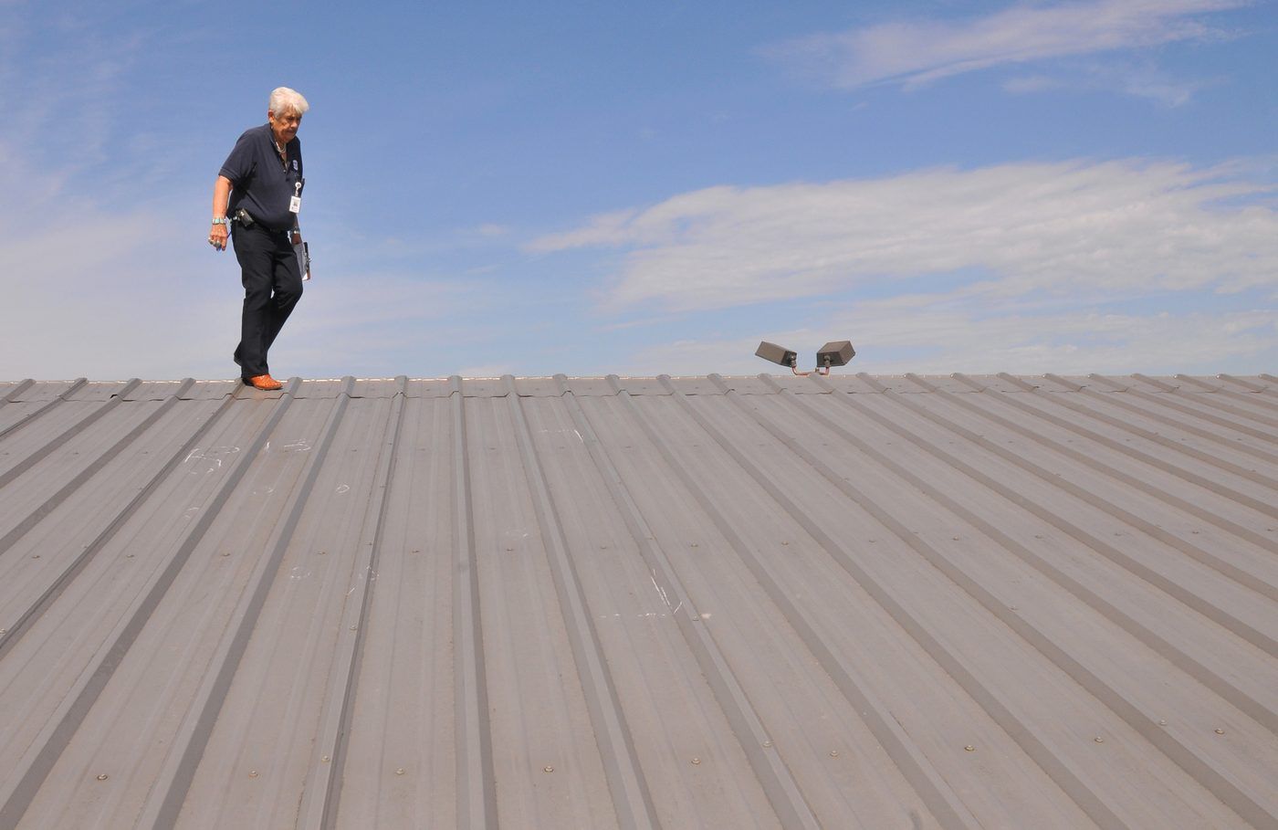 Inspector walking a metal roof with a clipboard, examining the field in daylight