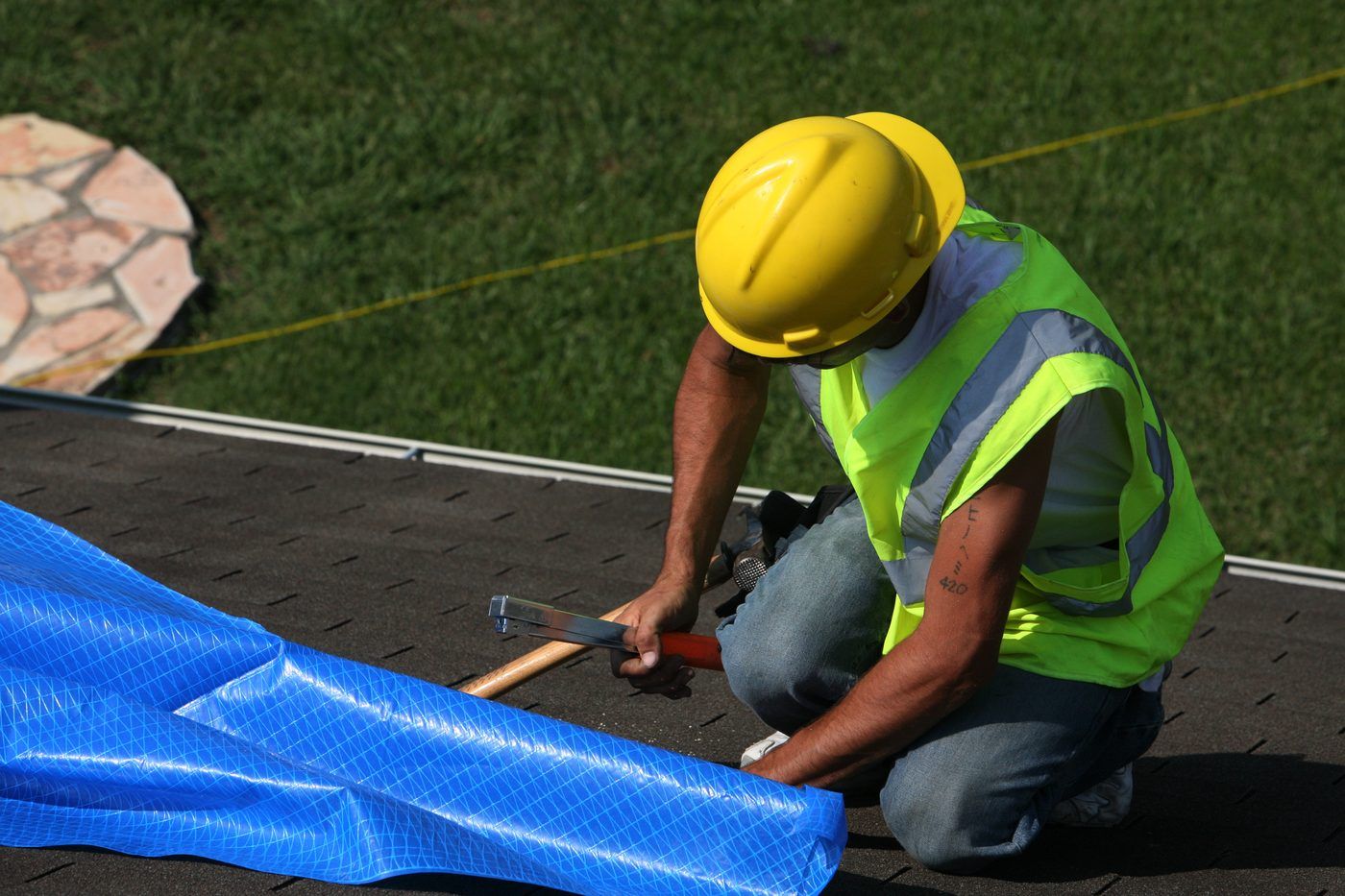 Worker securing a blue tarp on a residential shingle roof after storm damage