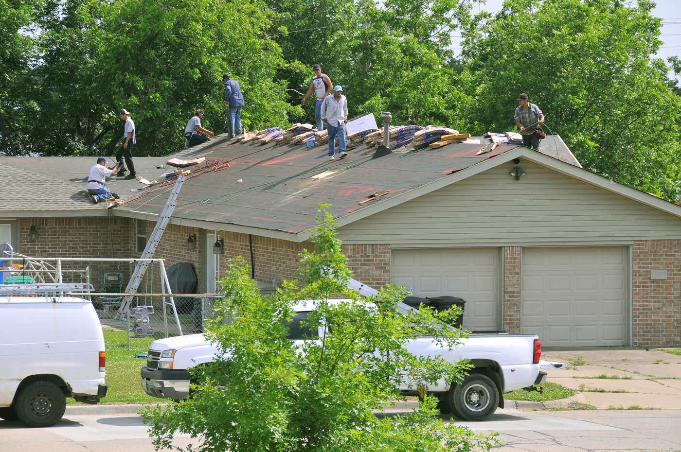 Crew removing old shingles during a residential roof replacement, with new shingle bundles on the ridge