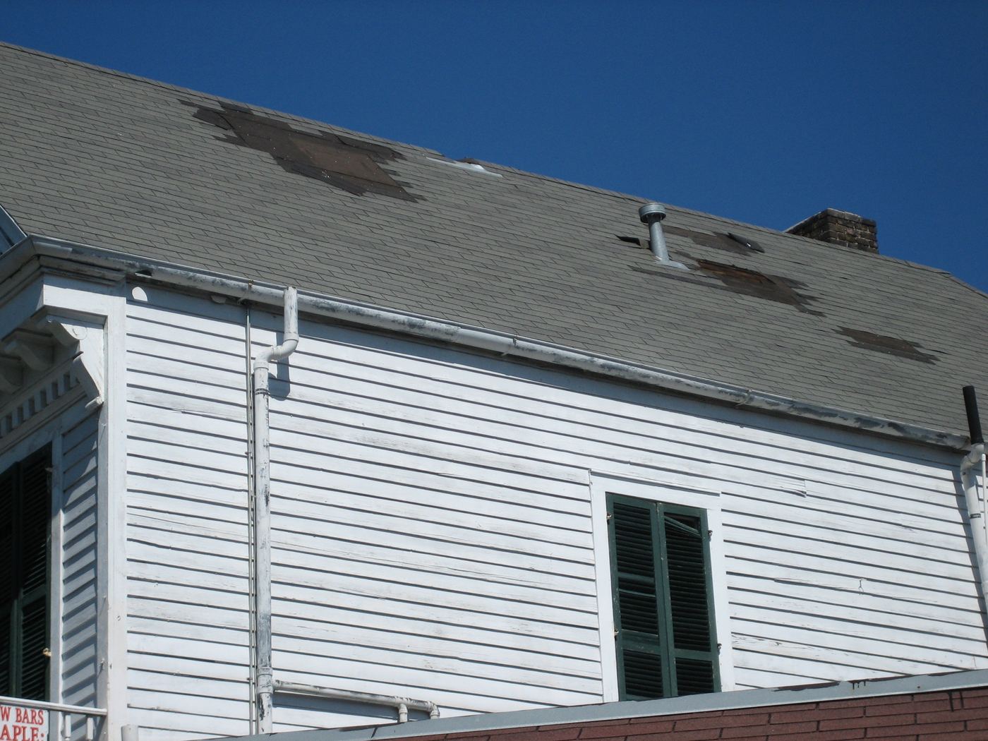 Gray asphalt shingle roof with missing courses exposing dark underlayment around a roof vent